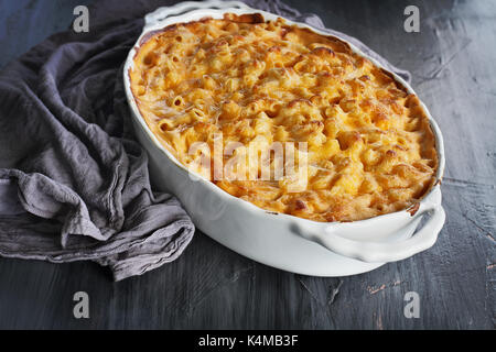 Hohe Engel Blick auf einen Teller von frisch gebackenen Makkaroni und Käse mit Tischdecke und altes Holz Löffel über einen rustikalen dunklen Hintergrund. Stockfoto