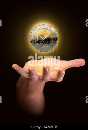 Eine männliche Hand beschwört eine schwimmende monero cryptocurrency Hologramm in Gold und Silber physisch Münze Form auf einem dunklen Studio Hintergrund Stockfoto