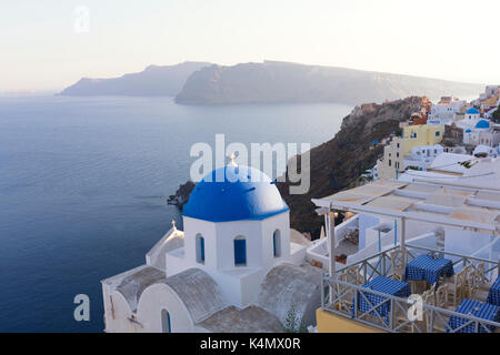 Abendlicher Blick auf die Caldera in Oia mit blauen Kuppelkirche und entfernten vulkanischen Klippen, Santorini, griechische Inseln, Griechenland, Europa Stockfoto