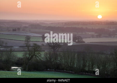 Erhöhten Blick auf die hügelige Landschaft, die Sonne über der Stadt Northampton in der Ferne an einem frostigen Morgen, Northamptonshire, England. Stockfoto
