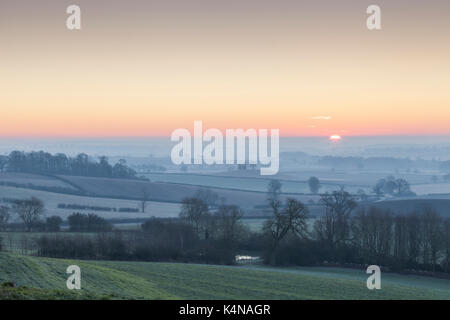 Nebel und Frost über die hügelige Landschaft als Morgendämmerung bricht an einem kalten Januar morgen in Richtung Northampton in Northamptonshire, England suchen. Stockfoto