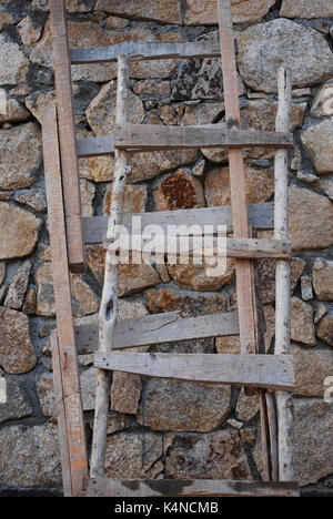 Rustikale Holzleitern gegen eine Mauer aus Stein Stockfoto