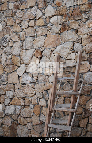 Rustikale Holzleitern gegen eine Mauer aus Stein Stockfoto