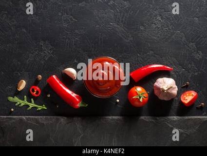 Tomatensauce in der Schüssel und jar auf schwarzem Hintergrund Textur Stockfoto