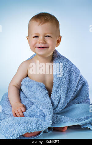 Acht Monate altes Baby nach dem Waschen sitzen in großen weichen Handtuch und lächelnd auf Weißem und Blauem Hintergrund Stockfoto