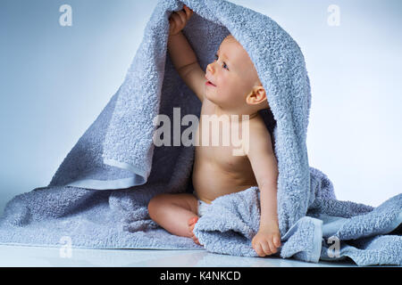 Acht Monate altes Baby nach dem Waschen sitzen in großen weichen Handtuch und lächelnd auf Weißem und Blauem Hintergrund Stockfoto