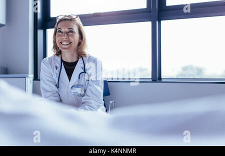 Gerne Ärztin im Krankenhaus Zimmer sitzen. Arzt im Krankenhaus lächelnd. Stockfoto
