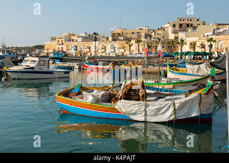 MARSAXLOKK, MALTA - 23. AUGUST 2017: Traditionelle bunte Luzzu Fischerboote ankommen und Verankerung in den frühen Morgen im Hafen von Marsaxlokk Stockfoto
