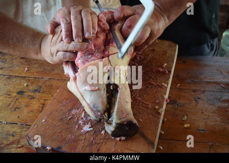 Männliche Hände sägen ein rohes Schweine Kopf in die Hälfte Stockfoto