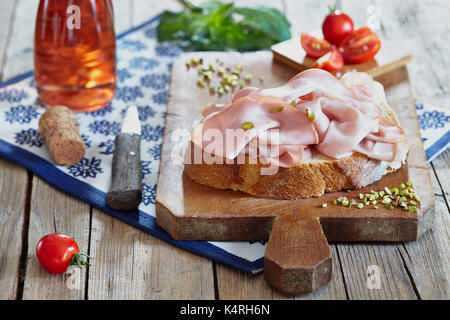 Mortadella mit Pistazien auf das Brot in Scheiben schneiden, mit Cherry Tomaten und Rose Sekt. Stockfoto