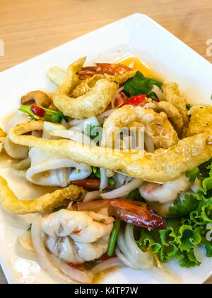 Thailändische Küche: Yum Sam Krob, knusprigem Fisch Maw, frittierter Tintenfisch und Garnelen in der würzigen Gemischt Cashewnuß-Salat in weißer Teller am Tisch Hintergrund Stockfoto