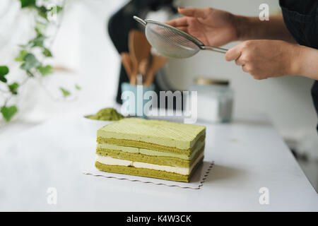 Gießen grüner Tee Pulver über leckeren Käsekuchen Stockfoto