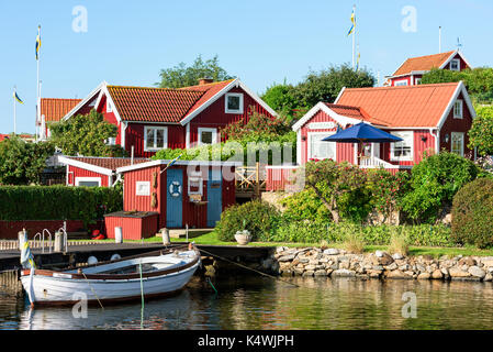 Karlskrona, Schweden - 28. August 2017: Reisedokumentation der Stadt Umgebung. Rot und Weiß traditionelle Küste Ferienhäuser Kabinen und angelegtes Boot i Stockfoto