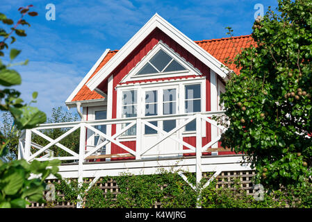 Rote und weiße Blockhaus Giebel mit Balkon von Obstbäumen und Sträuchern umgeben. Stockfoto