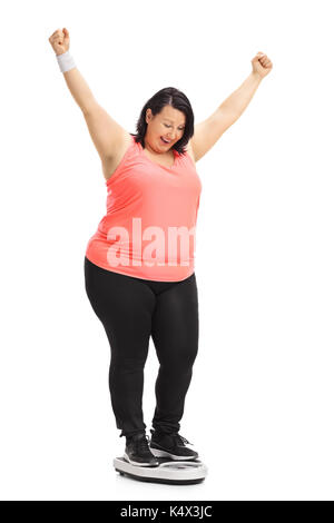 Voller Länge Porträt einer übergewichtigen Frau auf einer Waage stehen und gestikulierte Glück isoliert auf weißem Hintergrund Stockfoto