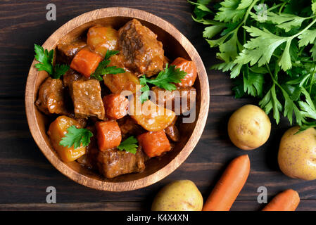 Fleisch-Eintopf mit Gemüse in Schüssel auf hölzernen Hintergrund, Ansicht von oben Stockfoto