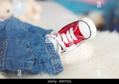 Modischen roten Sneakers auf dem kleinen neugeborenen Baby jungen Füße, baby boy Jeans und Turnschuhe Stockfoto