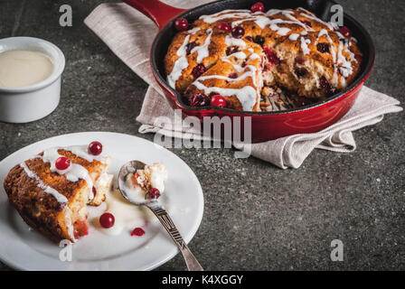 Britisches Englisch traditionelles Gebäck. Cookies Torte cranberry Scones mit Orangenschalen, mit süßen weißen Glasur, in eine Pfanne geben und auf einem Teller. Schwarz sto Stockfoto