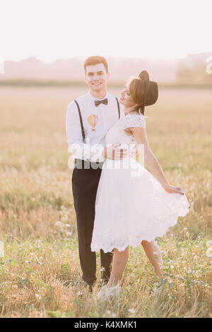 Die schöne Aussicht auf das jungvermählte Paar umarmen im Feld. Die Braut ist das Spielen mit Ihrem weißen vintage Wedding Dress. Stockfoto