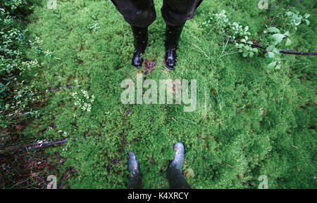 Männliche und weibliche Füße in Gummistiefel in dicken Moss Stockfoto