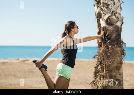 Seite Porträt der jungen Sportlerin und lehnte sich gegen den Baum Stretching Stockfoto