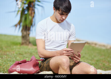 Portrait des jungen Mannes draußen sitzen mit Tablet Stockfoto