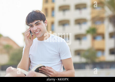 Porträt der jungen glücklich Mann auf mobilen und Holding Buch Stockfoto