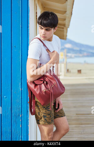 Portrait der junge Mann lehnte sich gegen die Wand mit Rucksack Stockfoto