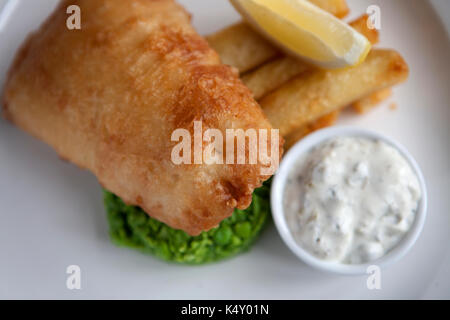Zerschlagene Fisch und Chips mit Erbsenpüree und Sauce Tartar auf einer Platte Stockfoto