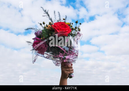 Ein Blumenstrauß in der Hand auf blauen Himmel Hintergrund. Hand des Kindes ist ein Geschenk ein Bouquet von schönen Blumen am 1. September. Stockfoto