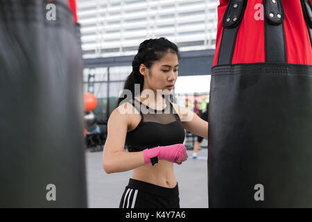 Junge Frau ausführen Übung im Fitnesscenter. weiblichen Athleten schlagen und Stanzen Sandsack mit Rudergerät in Boxing Gym. Sportlich asiatischen Mädchen worki Stockfoto