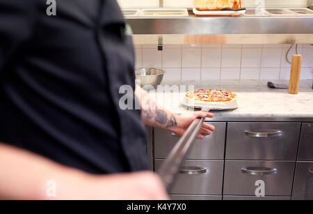 Koch oder Bäcker mit Pizza auf der Schale in der Pizzeria Stockfoto