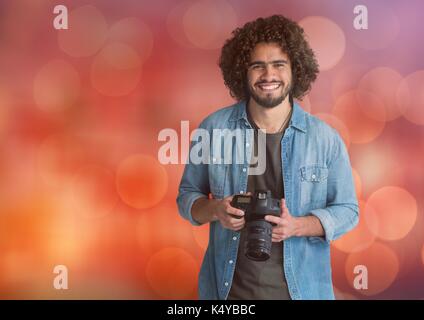 Digital composite Der glückliche junge Fotograf mit der Kamera auf die Hände. Red bokeh Hintergrund Stockfoto