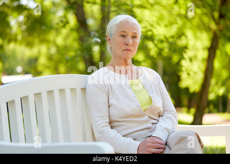 Traurige ältere Frau sitzt auf der Bank im Park Stockfoto