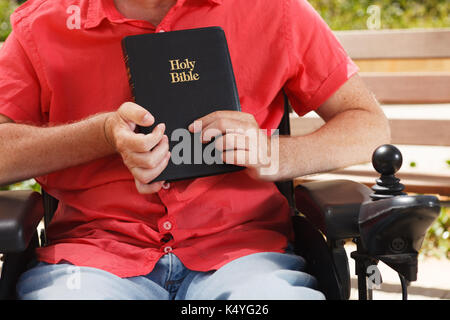 Bibel in den Händen von behinderten Menschen im Rollstuhl. Stockfoto