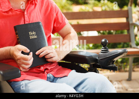 Bibel in den Händen von behinderten Menschen im Rollstuhl. Stockfoto