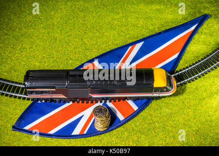 Ein Modell der Bahn und Schiene auf Union Jack Farben, von einer Wiese umgeben, mit neuen 1 Pfund Sterling Pound Münzen. Konzept der britischen Bahn Reisen und die damit verbundenen Kosten. Stockfoto