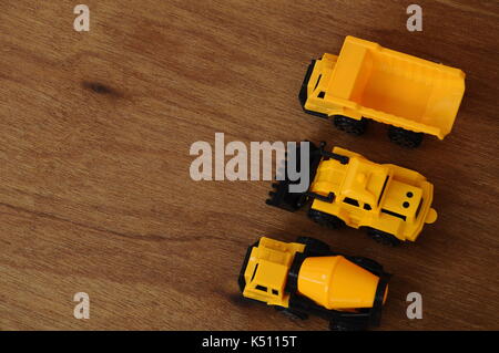 Gruppe von kleinen schwere Baumaschine Spielzeug, Lkw, Bulldozer und Betonmischer. Alle aus Kunststoff auf einer Holzmaserung Textur Hintergrund isoliert. Stockfoto