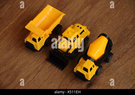 Gruppe von kleinen schwere Baumaschine Spielzeug, Lkw, Bulldozer und Betonmischer. Alle aus Kunststoff auf einer Holzmaserung Textur Hintergrund isoliert. Stockfoto