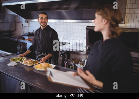 Junger Kellner Essen zubereiten, während an der Kellnerin im Café suchen Stockfoto