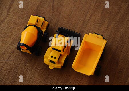 Gruppe von kleinen schwere Baumaschine Spielzeug, Lkw, Bulldozer und Betonmischer. Alle aus Kunststoff auf einer Holzmaserung Textur Hintergrund isoliert. Stockfoto