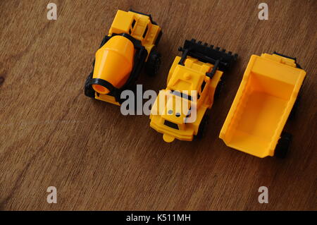 Gruppe von kleinen schwere Baumaschine Spielzeug, Lkw, Bulldozer und Betonmischer. Alle aus Kunststoff auf einer Holzmaserung Textur Hintergrund isoliert. Stockfoto