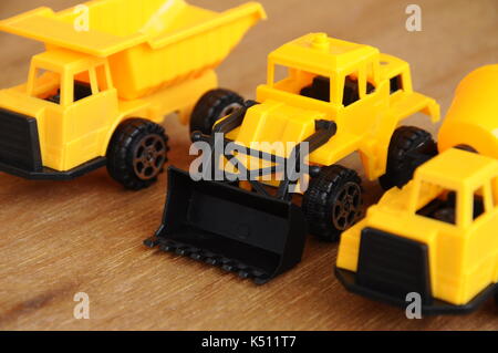 Gruppe von kleinen schwere Baumaschine Spielzeug, Lkw, Bulldozer und Betonmischer. Alle aus Kunststoff auf einer Holzmaserung Textur Hintergrund isoliert. Stockfoto