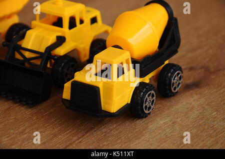 Gruppe von kleinen schwere Baumaschine Spielzeug, Lkw, Bulldozer und Betonmischer. Alle aus Kunststoff auf einer Holzmaserung Textur Hintergrund isoliert. Stockfoto