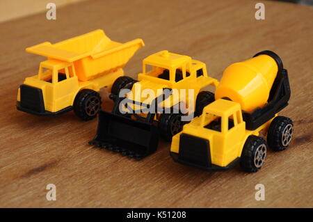 Gruppe von kleinen schwere Baumaschine Spielzeug, Lkw, Bulldozer und Betonmischer. Alle aus Kunststoff auf einer Holzmaserung Textur Hintergrund isoliert. Stockfoto