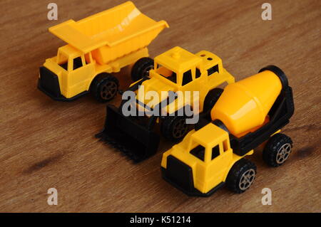 Gruppe von kleinen schwere Baumaschine Spielzeug, Lkw, Bulldozer und Betonmischer. Alle aus Kunststoff auf einer Holzmaserung Textur Hintergrund isoliert. Stockfoto