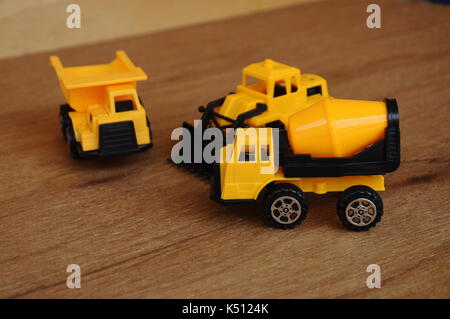 Gruppe von kleinen schwere Baumaschine Spielzeug, Lkw, Bulldozer und Betonmischer. Alle aus Kunststoff auf einer Holzmaserung Textur Hintergrund isoliert. Stockfoto