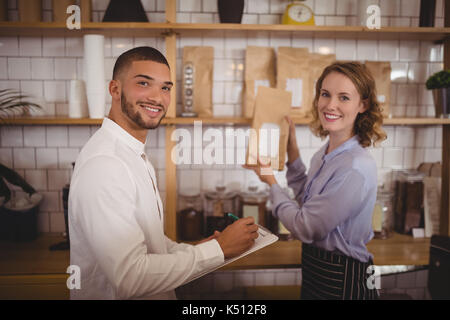 Portrait von lächelnden Mann Eigentümer und Kellnerin, die die Pakete auf dem Regal im Coffee Shop Stockfoto