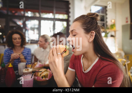 In der Nähe von schönen jungen Frau burger Essen im Coffee Shop Stockfoto