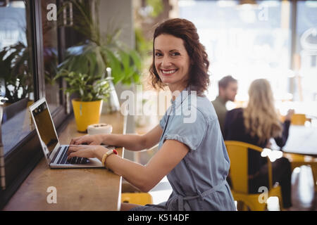 Portrait von lächelnden jungen Frau mit Laptop sitzen an der Theke im Café Stockfoto